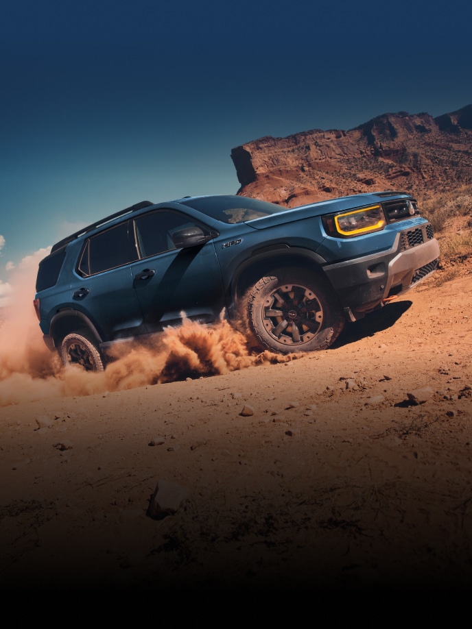 2027 Honda Passport TrailSport Elite in Smoke Blue Pearl profile driving through desert sand kicking up dust (Mid-Size SUV).