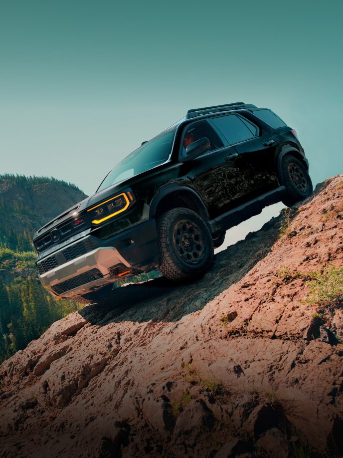 2026 Passport TrailSport Elite in Crystal Black Pearl carefully descends steep rocky hill with alpine trees in background. Driver's window is down in order to help navigate the terrain down.