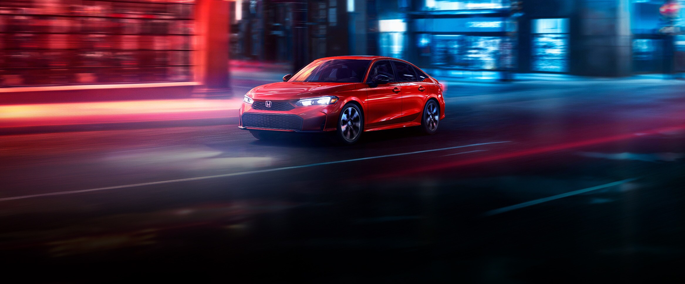 2027 Honda Civic Sedan Sport Hybrid in Rallye Red front driving on a city street at night (Compact Sedan).