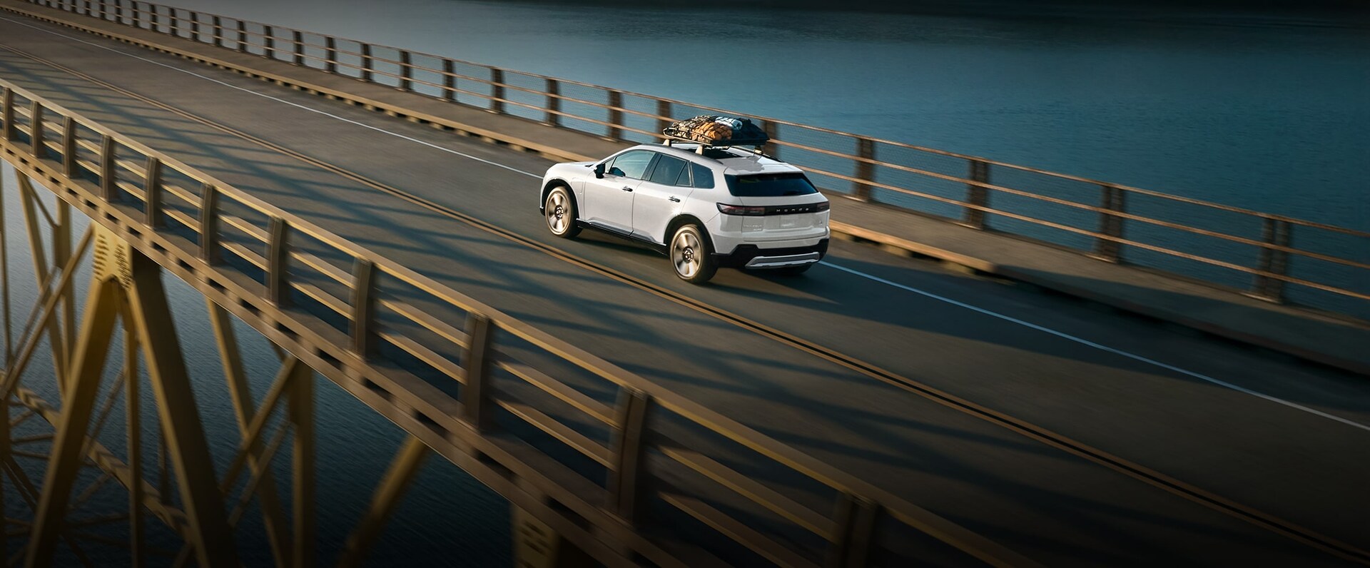 2025 Honda Prologue Elite shown with Honda Genuine Accessories* in Snowfall Pearl, is captured from a top view crossing a bridge.