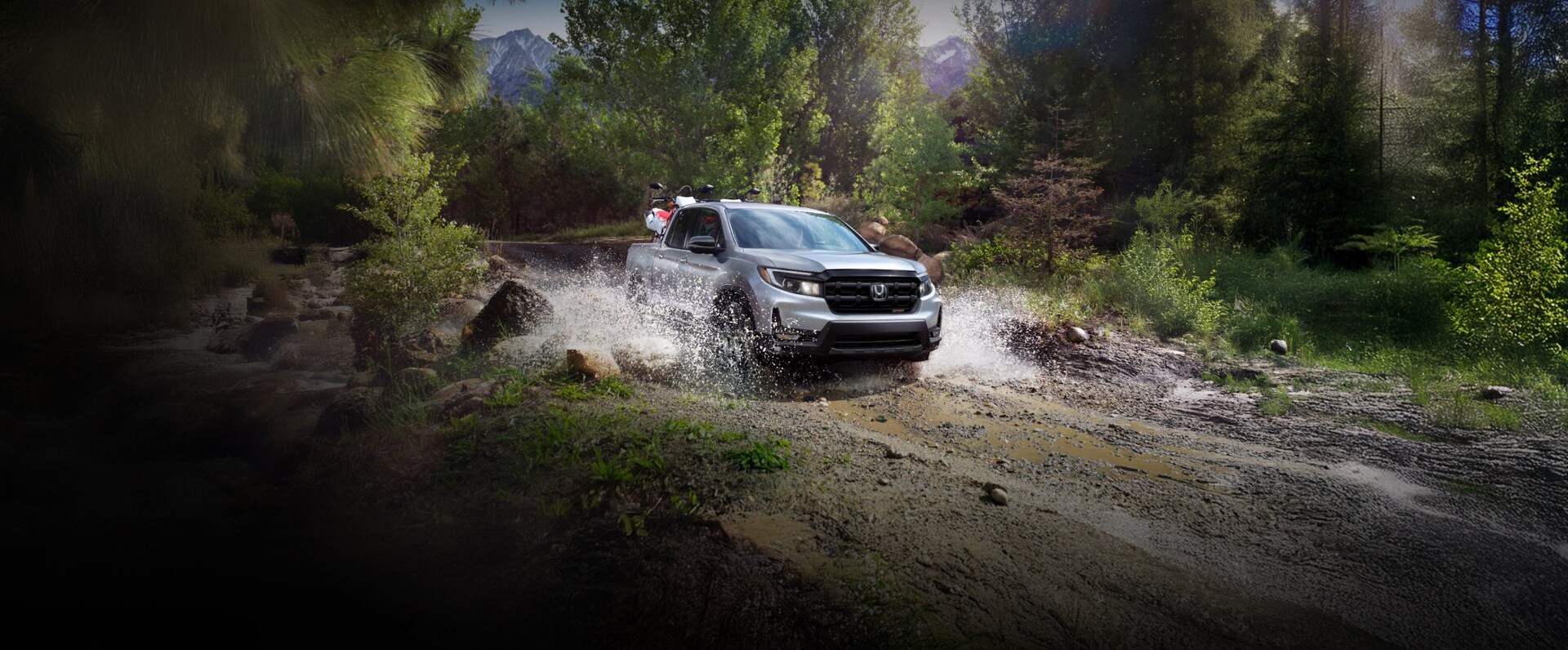 2025 Honda Ridgeline Sport in Solar Silver Metallic driving through water with dirt bikes in back.