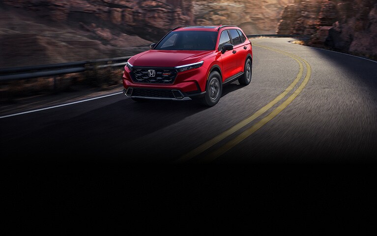 2027 Honda CR-V TrailSport Hybrid in Radiant Red Metallic front view driving on a canyon road (Compact Crossover SUV).