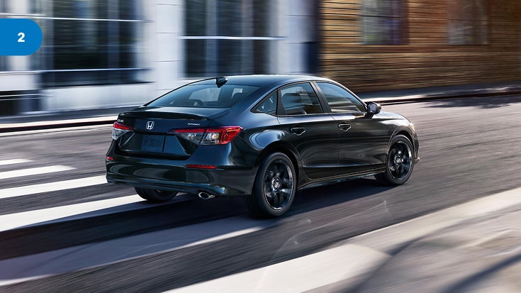 2022 Honda Civic Sedan in Crystal Black Pearl back driving through a modern city street (Compact Sedan).