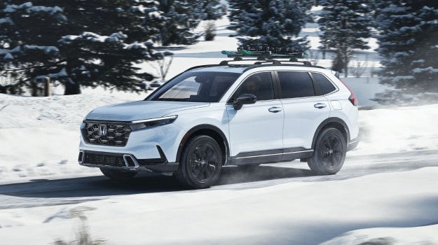 2026 Honda CR-V in Platinum White Pearl profile driving on a snowy road with skis on the roof (Full-Size SUV).