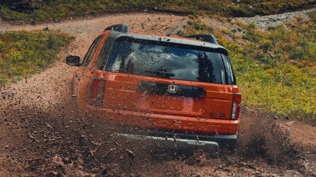 2027 Honda Passport TrailSport Elite in Orange Sunset back splashing through a deep muddy trail (Mid-Size SUV).