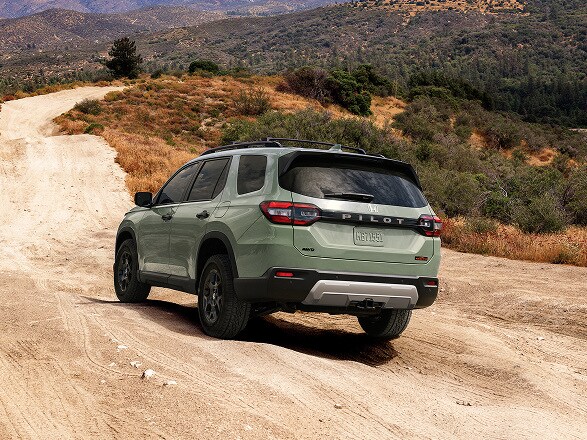 2026 Honda Pilot in Ash Green Metallic back driving on a winding dirt road in the mountains (Full-Size SUV).