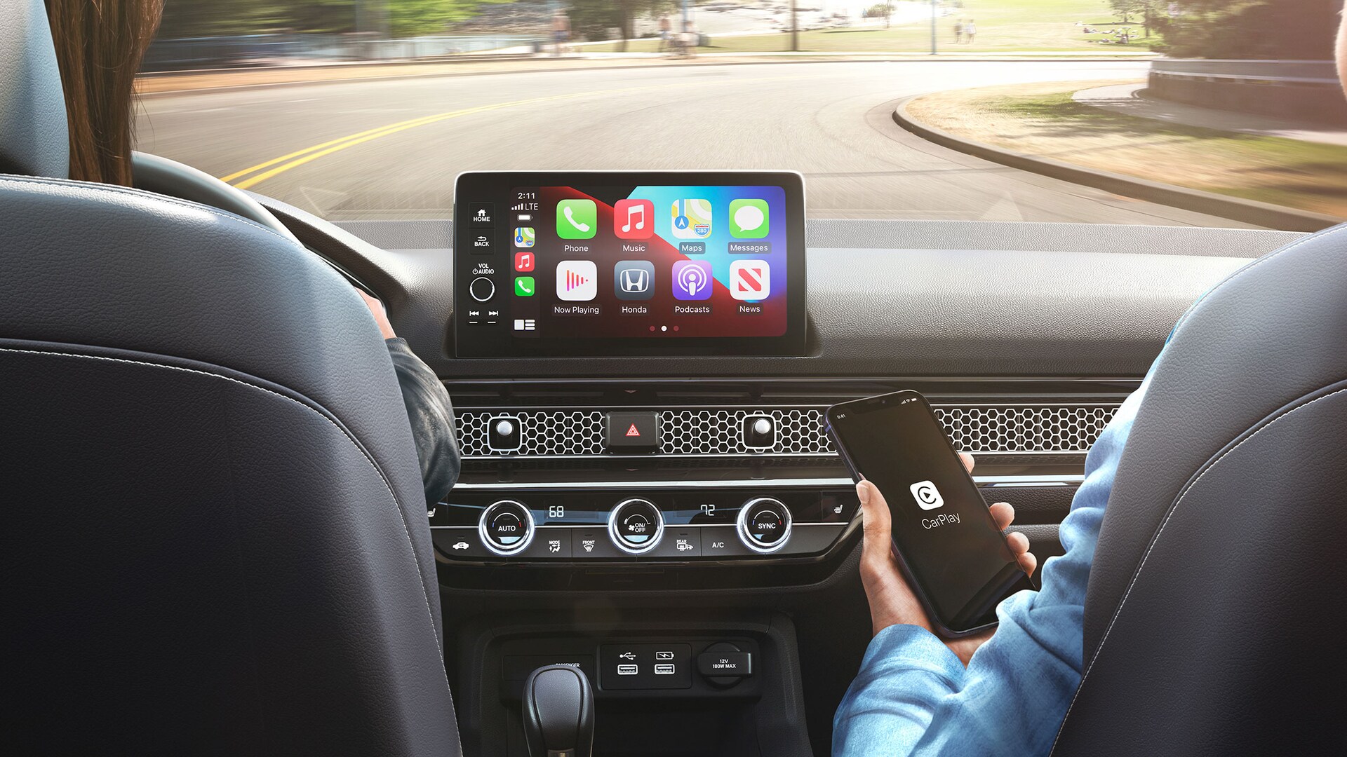 Apple CarPlay® menu on the 9-inch color touch-screen in the 2022 Honda Civic Sport Touring Hatchback with Black Leather, with front passenger holding an iPhone®.