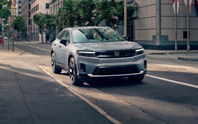 2024 Honda Prologue Elite shown in Sonic Gray Pearl parked curbside at urban café.
