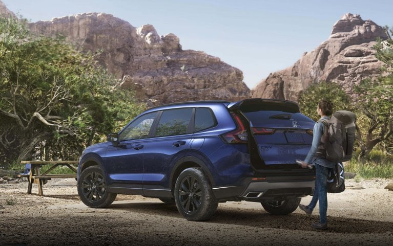 2026 Honda CR-V Sport Touring in Canyon River Blue Metallic parked at a campground in a desert canyon setting. A man uses his foot to activate the power tailgate.
