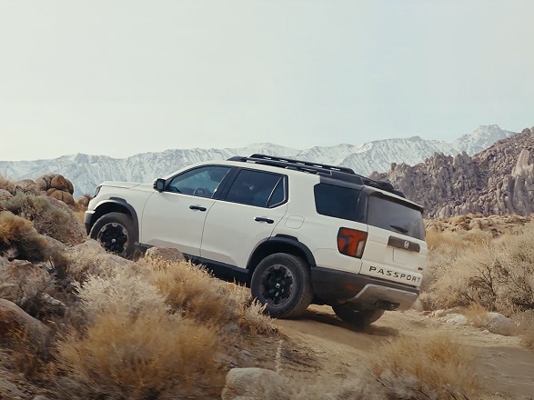 2026 Honda Passport Trailsport Elite in Platinum White Pearl profile driving up a rocky mountain trail (Mid-Size SUV).