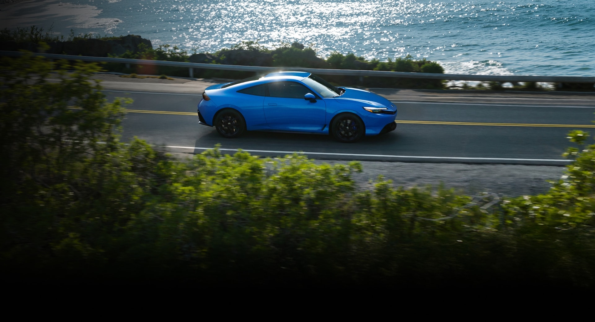 2026 Honda Prelude in Boost Blue Pearl driving through a costal road, profile view.