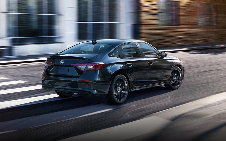 2026 Honda Civic Sedan Sport Hybrid in Crystal Black Pearl rear three-quarter view driving on a city street (Compact Sedan)