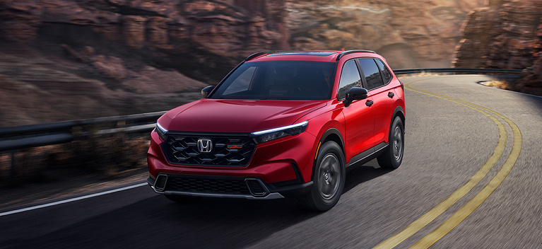 2027 Honda CR-V TrailSport Hybrid in Radiant Red Metallic front driving on a winding mountain road (Compact Crossover SUV).