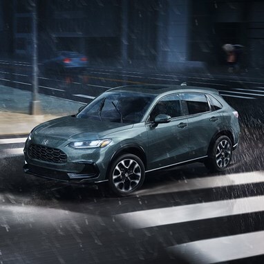 2027 Honda HR-V EX-L in Nordic Forest Pearl profile view driving on a rainy city street (Subcompact Crossover SUV).