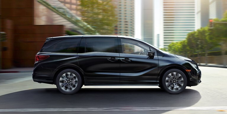 2027 Odyssey Elite family van in Crystal Black Pearl driving on a city street (Minivan).