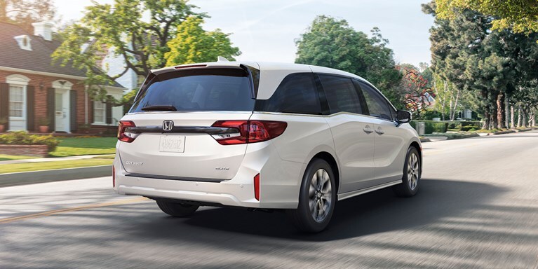 2027 Honda Odyssey Elite in Platinum White Pearl back driving through a sunny residential neighborhood (Minivan).