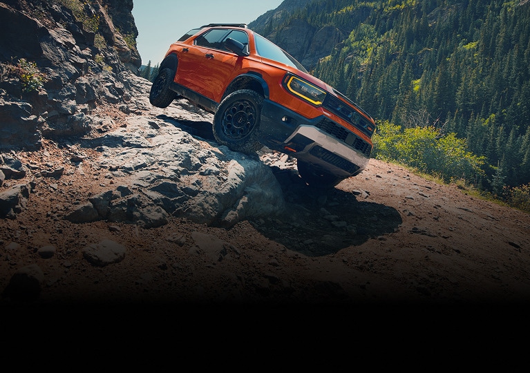2027 Honda Passport TrailSport Elite in Sunset Orange front navigating a steep rocky mountain trail (Mid-Size SUV).