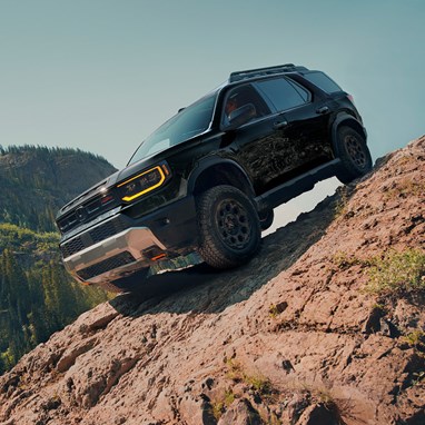 2027 Honda Passport TrailSport Elite in Crystal Black Pearl front driving up a steep rocky mountain slope (Mid-Size SUV).