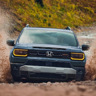 2027 Honda Passport TrailSport Elite in Smoke Blue Pearl front splashing through mud on an off-road trail (Mid-Size SUV).