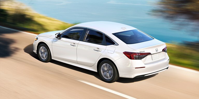 2027 Honda Civic Sedan LX in Platinum White Pearl rear three-quarter view driving on a coastal road (Compact Sedan)