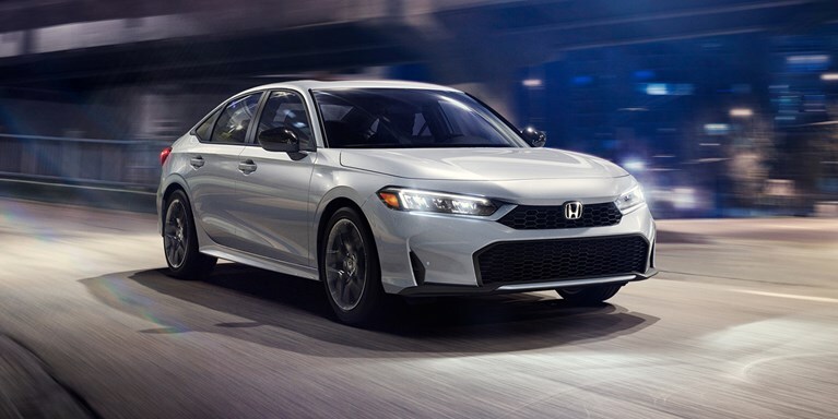 2027 Honda Civic Sedan Sport Hybrid in Solar Silver Metallic front three-quarter view driving on a street (Compact Sedan)