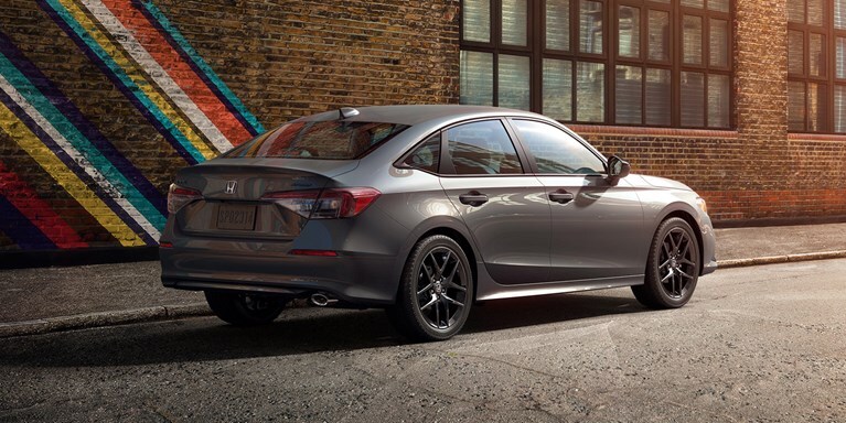 2027 Honda Civic Sedan Sport in Meteorite Gray Metallic rear three-quarter view parked on a city street (Compact Sedan)