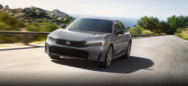2027 Honda Civic Sedan Sport Touring Hybrid in Urban Gray Pearl front driving along a scenic coastal road (Compact Sedan).