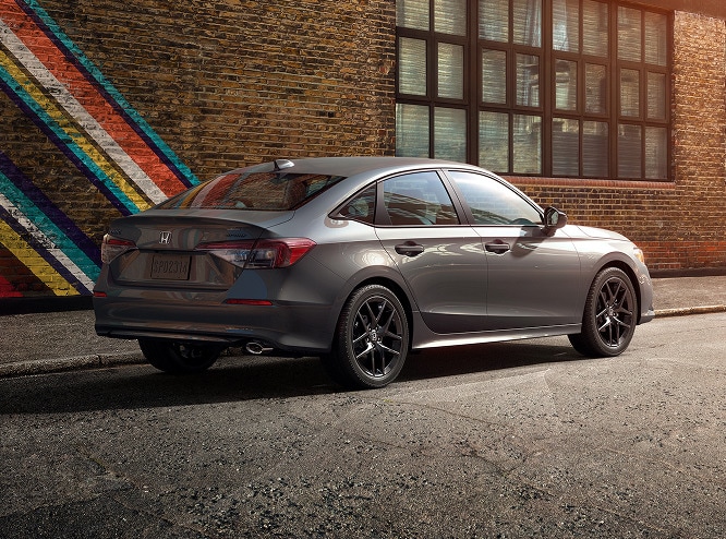 2027 Honda Civic Sedan Sport in Meteorite Gray Metallic rear three-quarter view parked on a city street (Compact Sedan)