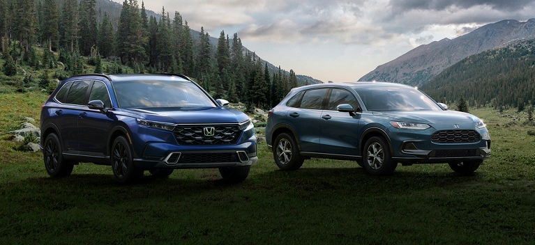 2026 Honda CR-V and Honda HR-V front in a scenic grassy mountain valley under a cloudy sky.