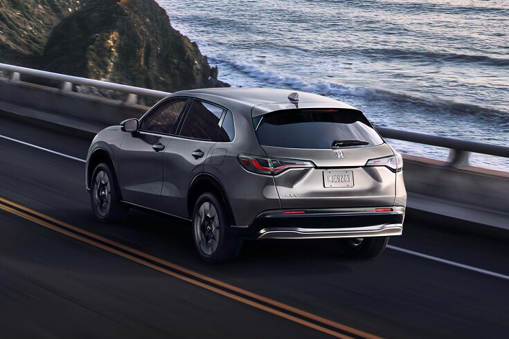 2026 Honda HR-V EX-L in Modern Steel Metallic back driving along a scenic coastal bridge (Subcompact Crossover SUV).