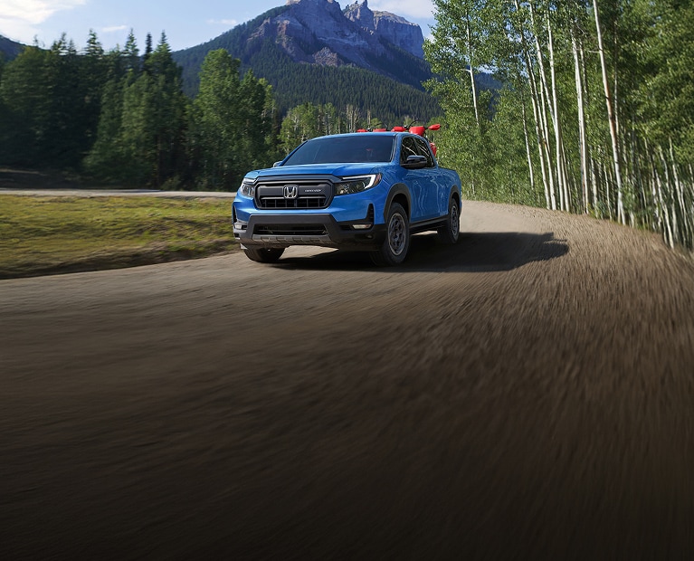 Honda Ridgeline Trailsport in Diffused Sky Blue Pearl with HPD Accessories Package driving on dirt road hauling two CRF motorbikes.